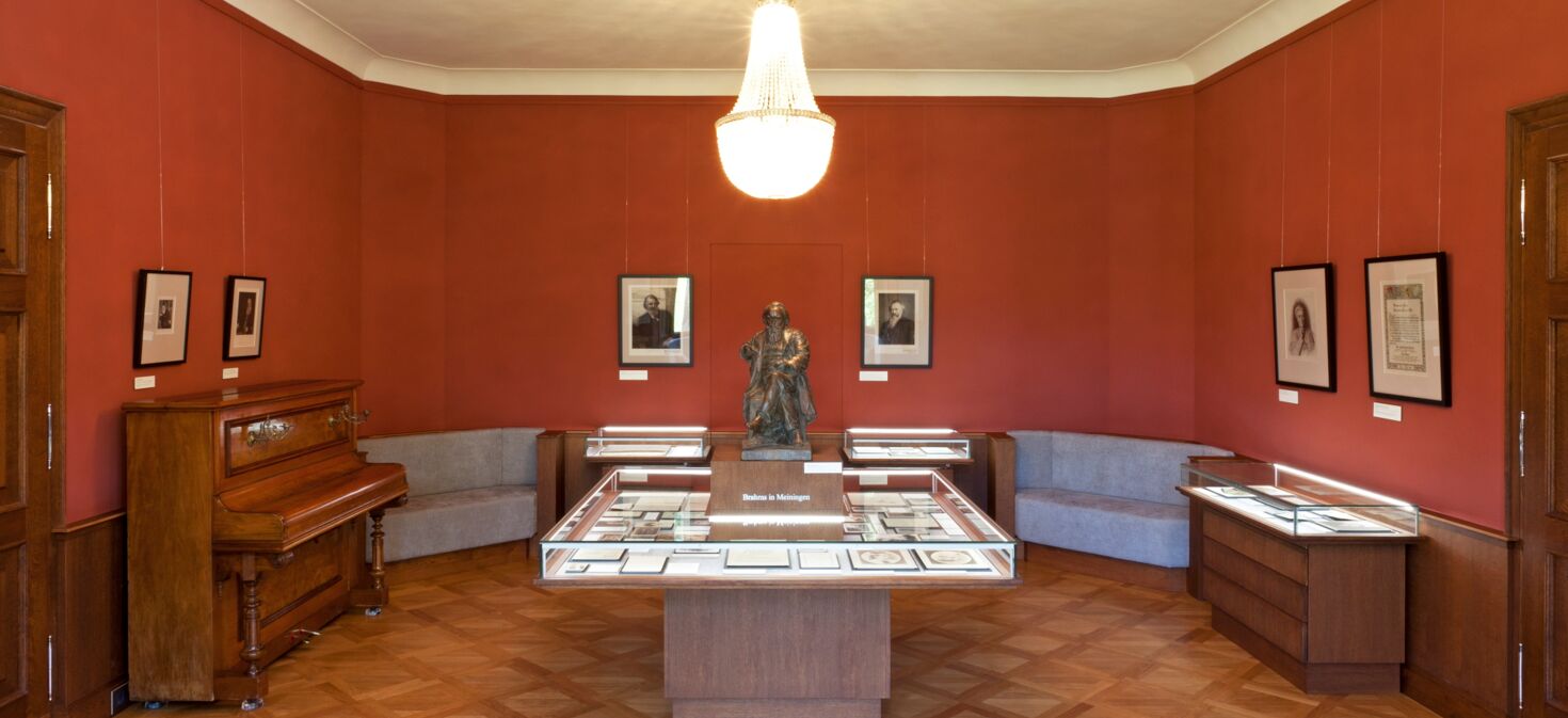 Innenaufnahme Brahms-Gedenkstätte im Schloss Altenstein mit Brahms-Statue, Klavier, Kronleuchter und Ausstellungsvitrinen